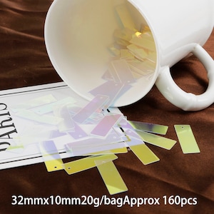 May include: A white ceramic mug spills iridescent rectangular sequins onto a brown surface. The sequins are approximately 32mm x 10mm and come in a bag of 20g, containing approximately 160 pieces. 32mmx10mm20g/bagApprox 160pcs