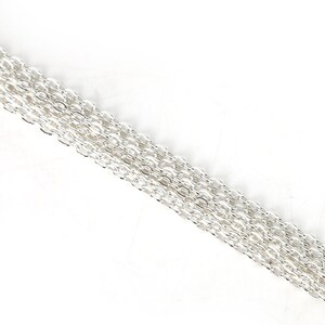 May include: A close-up of a silver chain, showing the individual links. The chain is lying flat on a white surface.
