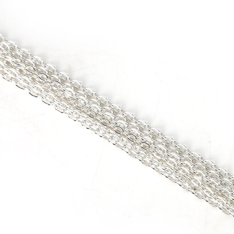 May include: A close-up of a silver chain, showing the individual links. The chain is lying flat on a white surface.