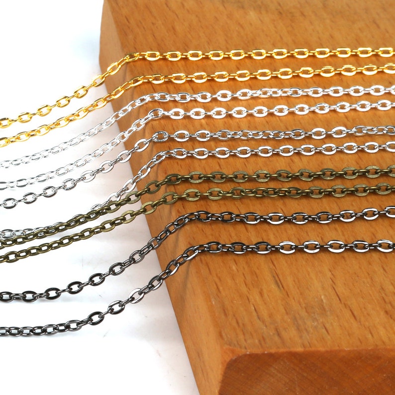 May include: Assortment of chain links in different colors, including gold, silver, black, and bronze. The chains are arranged in a row on a wooden surface.
