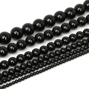 Peut inclure: Un ensemble de perles d'onyx noir de différentes tailles, disposées en rangées du plus grand au plus petit. Les perles sont lisses et polies, avec une finition brillante.