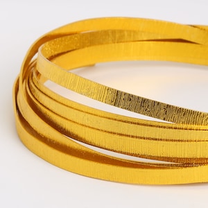 May include: A close-up of a gold metallic ribbon, coiled and ready for crafting projects. The ribbon has a textured surface, adding a touch of dimension.