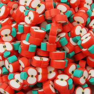 Puede incluir: Un montón de rodajas de arcilla polimérica con forma de manzana roja con detalles blancos y verdes. Las rodajas están cortadas para revelar el corazón de la manzana. Estas pequeñas piezas coloridas son ideales para manualidades y joyería.