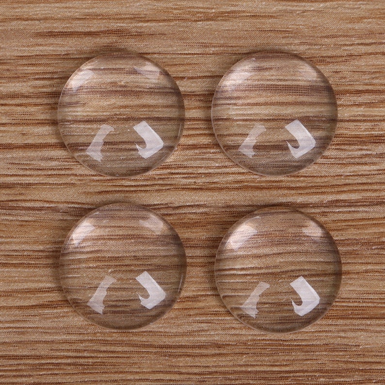May include: Four clear glass cabochons, each with a smooth, rounded surface, are arranged in a square pattern on a woodgrain background.