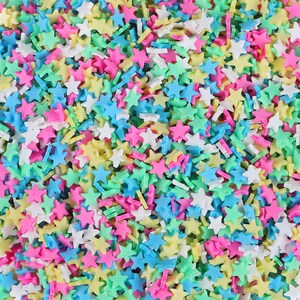 Puede incluir: Primer plano de una colorida variedad de chispas en forma de estrella. Las chispas son de varios colores pastel, incluyendo rosa, amarillo, azul, verde y blanco. Las estrellas están dispersas, creando una textura vibrante y juguetona.