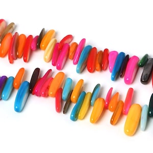 Può includere: Una fila di perline lunghe e ovali, lisce e lucide, di colori vivaci. Le perline sono disposte a spina di pesce e sono realizzate con materiali naturali. Le perline sono in tonalità di rosa, rosso, arancio, giallo, verde, blu e viola.