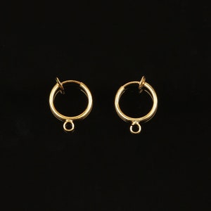 May include: A pair of gold-toned hoop earrings with a clip-on closure. The earrings have a small loop at the bottom.