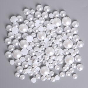 May include: A large collection of white pearl-like round beads. The beads are various sizes and are scattered on a gray background.