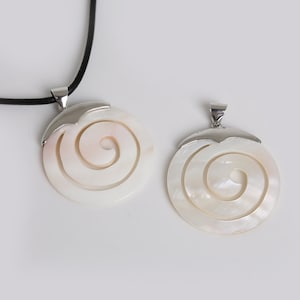 Könnte beinhalten: Zwei weiße Perlmutt-Anhänger mit silbernen Einstellungen. Die Anhänger haben ein Spiraldesign. Der größere Anhänger befindet sich an einer schwarzen Schnur.