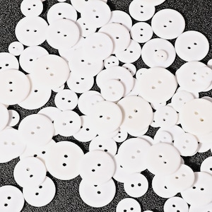 May include: A large collection of white round buttons of various sizes. The buttons have two holes each.