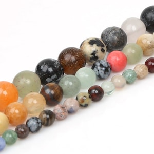 Puede incluir: Una hebra de cuentas de piedras preciosas de colores, incluyendo verde, marrón, negro, blanco, rojo y naranja. Las cuentas son redondas y lisas, y están enhebradas en un hilo transparente.