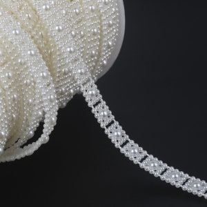 Puede incluir: Borde de perlas blancas con un patrón cuadrado. El borde está hecho de pequeñas perlas redondas que están cosidas juntas en un patrón repetitivo.