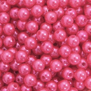 May include: A close-up image of a large quantity of pink pearl-like beads. The beads are round and have a smooth, shiny finish.