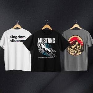 May include: Three t-shirts with different designs. The first t-shirt is white with the text "Kingdom Influence" in black and pink. The second t-shirt is black with a white horse graphic and the text "Mustang Fencing Club". The third t-shirt is gray with a red, white, and blue mountain graphic.