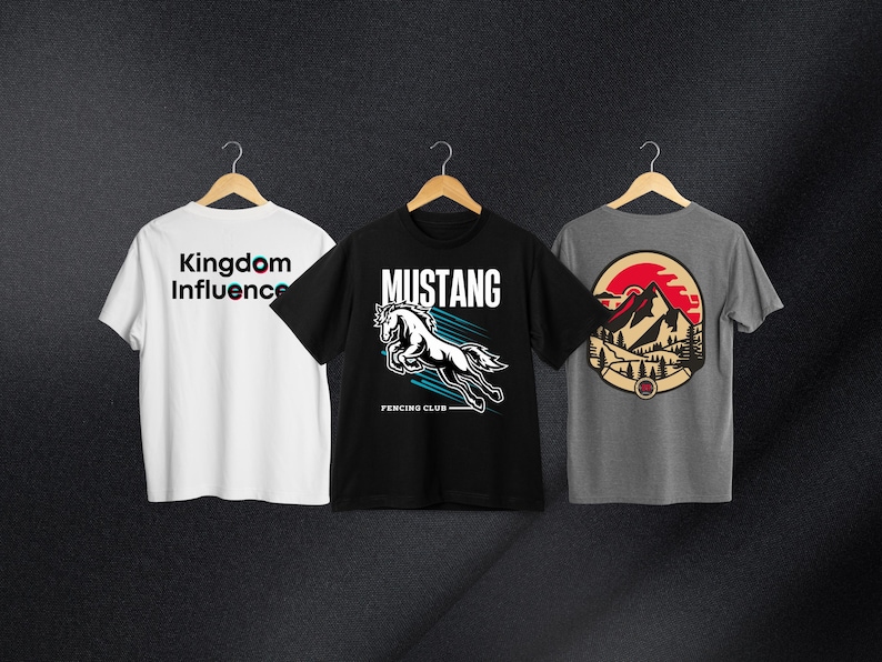 May include: Three t-shirts with different designs. The first t-shirt is white with the text "Kingdom Influence" in black and pink. The second t-shirt is black with a white horse graphic and the text "Mustang Fencing Club". The third t-shirt is gray with a red, white, and blue mountain graphic.