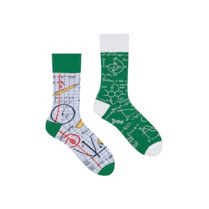 May include: A pair of green and white socks with a chalkboard pattern featuring maths equations, a pencil, a compass, and a DNA strand. The socks have a white cuff and a green heel and toe.