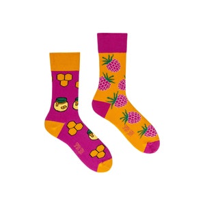 May include: A pair of patterned socks. One sock displays a honeycomb and honey jar design on a purple background, the other features raspberries on an orange background. The socks have magenta cuffs, heels, and toes.