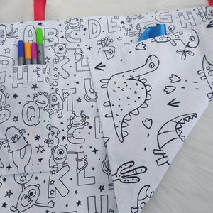Può includere: Una borsa tote in tela bianca con una stampa in bianco e nero di lettere, stelle e mostri. La borsa ha una tasca sul davanti con un nastro blu. La borsa è piegata a metà e l'interno è visibile. L'interno della borsa è bianco con una stampa in bianco e nero di dinosauri.