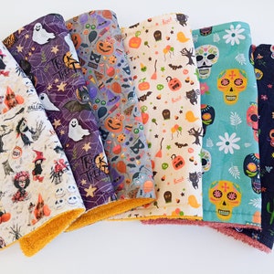 May include: Set of eight Halloween-themed fabric squares with various patterns, including skulls, pumpkins, bats, and ghosts. The fabric squares are all in different colours, including black, white, orange, purple, and green. The fabric squares are all trimmed with a yellow and orange fabric border.