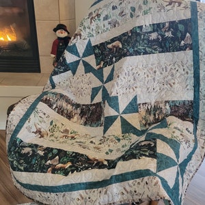 May include: A teal and white quilt with a woodland animal print. The quilt features a repeating pattern of pine trees, deer, and other forest creatures. The quilt is made of soft, comfortable fabric and is perfect for adding a touch of nature to any room.