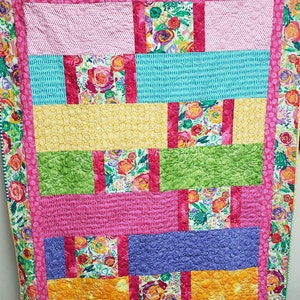 May include: A colorful patchwork quilt with a floral pattern. The quilt is made up of squares and rectangles of different colors and patterns, including pink, yellow, green, blue, and purple. The quilt is quilted with a simple stitch pattern.