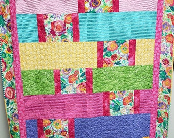 Könnte beinhalten: Ein farbenfroher Patchwork-Deckenbezug mit Blumenmuster. Der Bezug besteht aus Quadraten und Rechtecken in verschiedenen Farben und Mustern, darunter Rosa, Gelb, Grün, Blau und Lila. Der Bezug ist mit einem einfachen Steppmuster gesteppt.