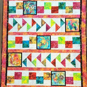 May include: A rectangular quilt featuring a vibrant orange and pink batik border. The quilt displays alternating rows of colorful batik squares, white fabric strips, and triangular patterns, interspersed with five square animal-themed panels.