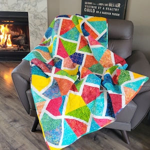 Könnte beinhalten: Eine bunte Patchwork-Decke mit geometrischem Muster in Blautönen, Grün, Rot, Gelb und Weiß. Die Decke ist gefaltet und über einen braunen Ledersessel gelegt.