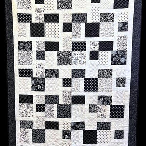 May include: Black and white quilt with a patchwork design. The quilt is made up of squares of different fabrics, each with a different pattern. The quilt is quilted with a simple stitch.