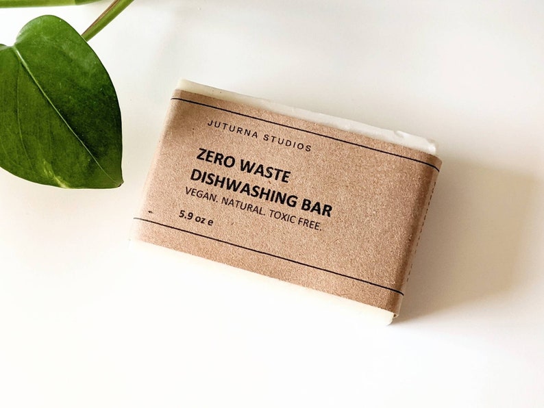 May include: A brown paper-wrapped bar of dish soap with the text "JUTURNA STUDIOS ZERO WASTE DISHWASHING BAR VEGAN. NATURAL. TOXIC FREE. 5.9 oz e" printed on the label.
