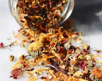 May include: A glass jar filled with dried flower petals and herbs, spilling out onto a white surface. The petals are a mix of orange, yellow, red, and white.