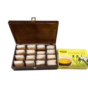 May include: A wooden tea box with a hinged lid, filled with individually wrapped tea bags. Next to the box is a yellow box of Jasmine Tea, with text and a picture of tea in a cup.