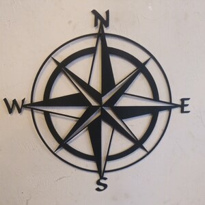 May include: Black metal compass with a star design and the cardinal directions N, S, E, and W.