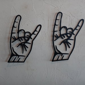 May include: Two black metal wall decor pieces in the shape of a hand making the rock and roll hand gesture.
