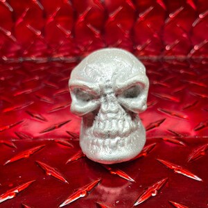 May include: A silver skull-shaped gear shift knob. The knob is detailed with a textured surface and a menacing expression.