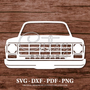 Peut inclure: Silhouette blanche d'un pick-up classique avec une calandre, des phares et un pare-brise. L'image est sur un fond en bois.