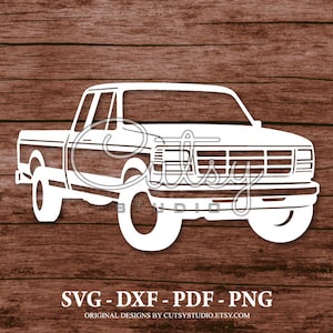May include: White silhouette of a pickup truck on a brown wood background. The truck has a large grille and a long bed. The image includes the text "SVG - DXF - PDF - PNG" and "ORIGINAL DESIGNS BY CUTSYSTUDIO.ETSY.COM".