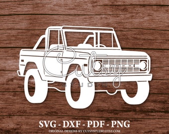 May include: White silhouette of a classic Ford Bronco truck with a black grille and large tires. The truck is on a wood background.