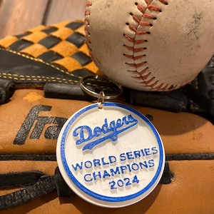 May include: A white and blue baseball keychain with the text "Dodgers World Series Champions 2024".
