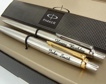 May include: Two silver Parker pens in a gift box. The top pen is engraved with "Happy Birthday" and the bottom pen is engraved with "John Smith".