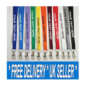 May include: A collection of eleven flat fabric lanyards in various colours including blue, purple, green, yellow, orange, maroon, red, white, grey, and black. Each lanyard features the white text YOUR TEXT HERE and a silver metal swivel hook.