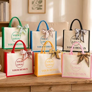 以下が含まれることがあります： 緑、青、黒、赤、黄、ピンクの持ち手と縁取りが付いた6つの長方形のキャンバストートバッグ。各バッグには、YOUR LOGOおよびYOUR DESIGNというテキストが記された円形のロゴエリアがあり、持ち手には柄入りのリボンが結ばれています。