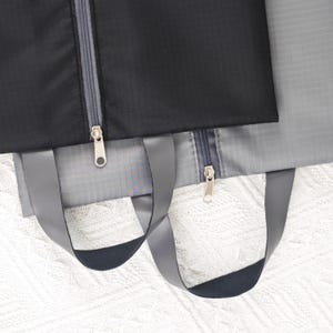 May include: Two gray and black zippered travel bags with black handles. The bags are made of a water-resistant material.