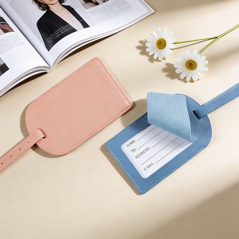 May include: A light pink luggage tag and a blue luggage tag with a matching blue strap. The blue tag features a liftable flap revealing a white information card with printed lines for Name, Tel, Address, and E-mail details for identification.