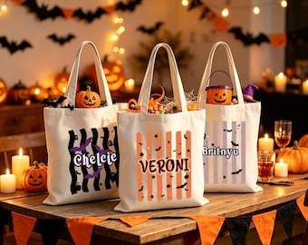 May include: Three off-white canvas tote bags featuring Halloween-themed designs. The first bag has black wavy stripes and purple bats with the name Chelcie. The second has orange stripes, bats, and stars with the name Veroni. The third has purple stripes and the name Britnyu.