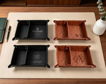 May include: Four rectangular valet trays with snap-button corners and internal dividers. Two trays are black with custom engravings, and two are brown with a textured finish featuring engraved initials and decorative flourishes.