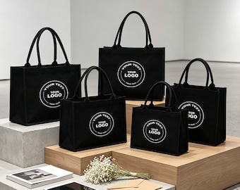 May include: Five black rectangular tote bags of varying sizes, each featuring a circular white graphic with the text "YOUR TEXT YOUR LOGO" printed in the center. The bags have two sturdy black handles and a structured, flat-bottomed design.