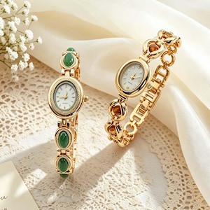 May include: Two gold-tone wristwatches with oval faces and white dials. One watch features a link bracelet accented with smooth, oval green stones. The second watch has a polished gold-tone link bracelet with an intricate, textured metal design.