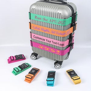 May include: A silver rolling suitcase with colorful luggage straps. The straps are green, orange, pink, and purple, with text that reads "Run the APU", "Catch Flights, Not Feelings", "Customize Your Text/Logo", and "Jet Set Go". Several luggage straps are also displayed separately.