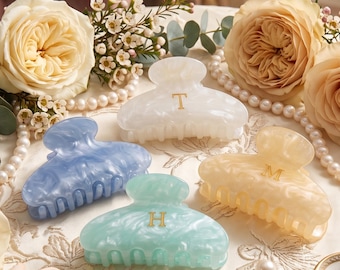 May include: Four hair claw clips in white, blue, light green, and beige, each featuring a marbled finish and a single gold letter monogram. The white clip displays the letter T, the beige clip displays M, and the light green clip displays H.